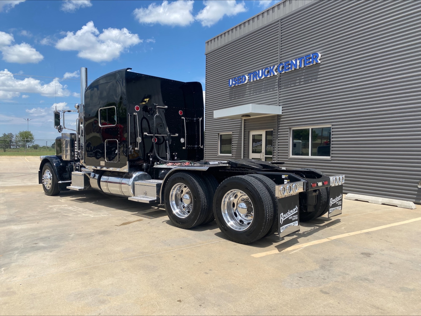 Peterbilt 389 tractor with black sleeper shows dual rear axle and chrome wheels outside truck center.
