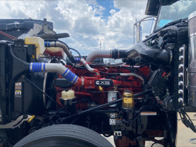 Peterbilt 389 engine bay with red X15 engine, visible blue silicone hoses, yellow coolant reservoir, and various metallic components.