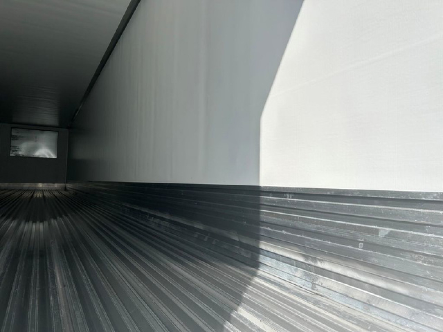 Trailer interior undercarriage view showing metal ribbed floor and side wall with a small window at far end