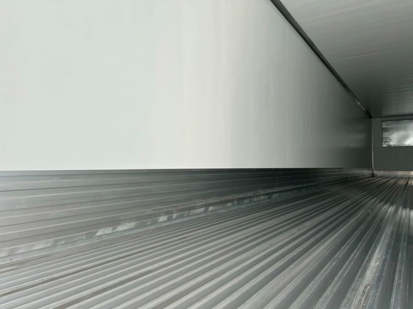 Interior of a refrigerated trailer cargo area with ribbed metal floor and side walls, empty and clean.