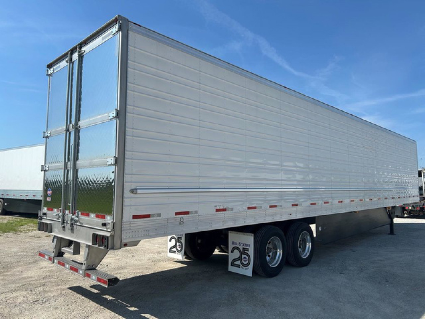 Utility refrigerated trailer shown from rear-left side with aluminum siding, tandem axles, rear doors, and reflective tape.