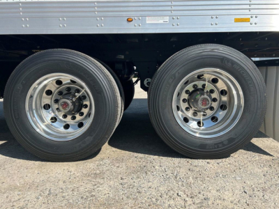 Dual rear wheels of a new 2027 Utility reefer trailer showing aluminum rims and tires, undercarriage with a side panel and small labeling.