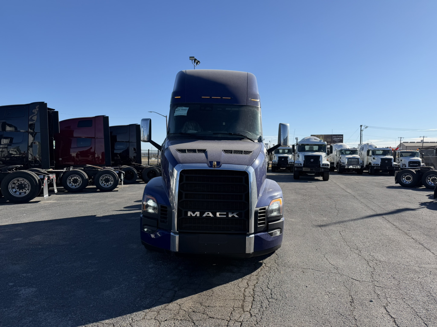 Front view of a blue 2026 Mack PR64T76H truck in a dealership lot with other trucks in background