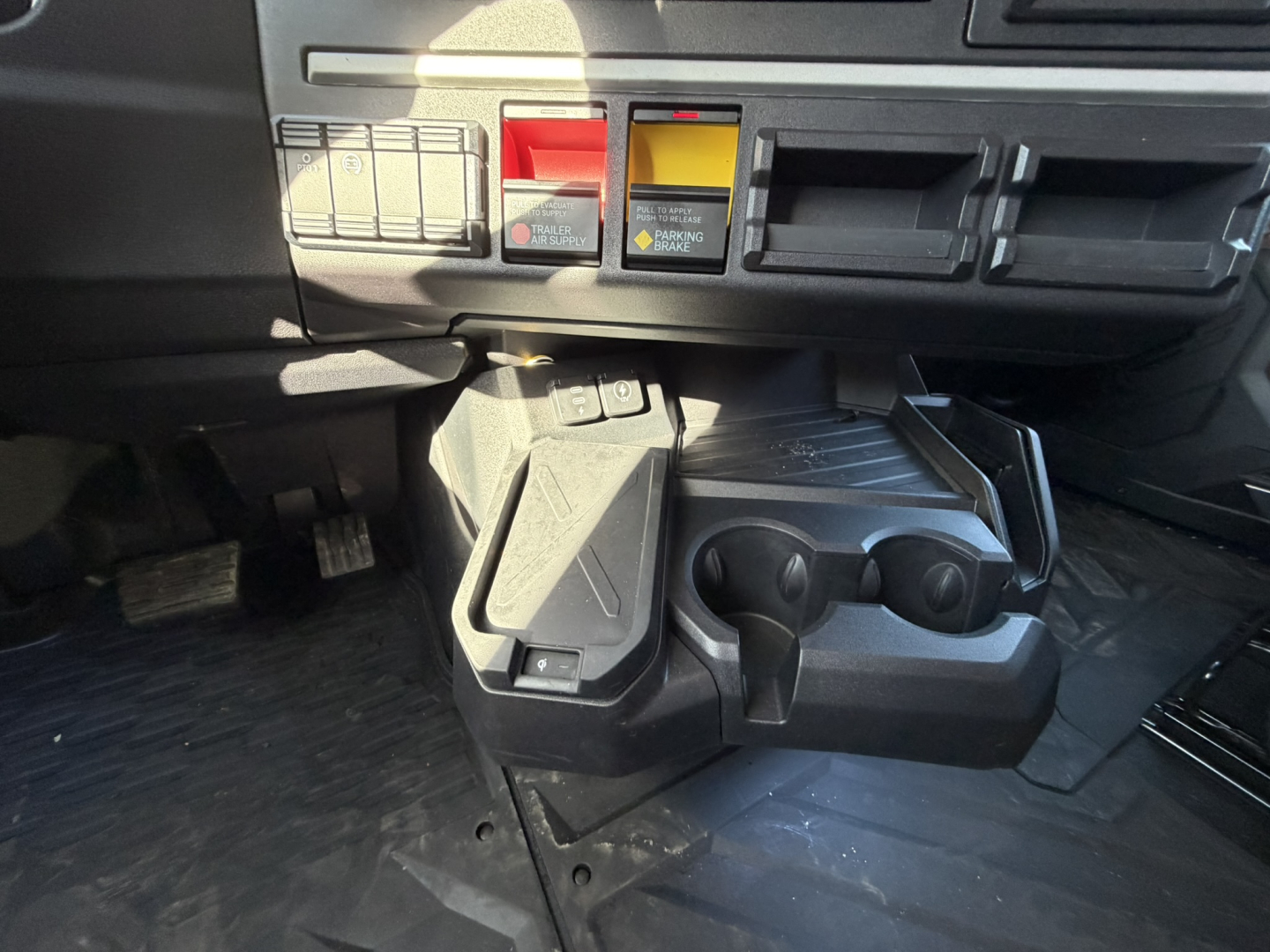 Mack PR64T76H truck interior center console area with cup holders and controls, dashboard switches, and pedals visible