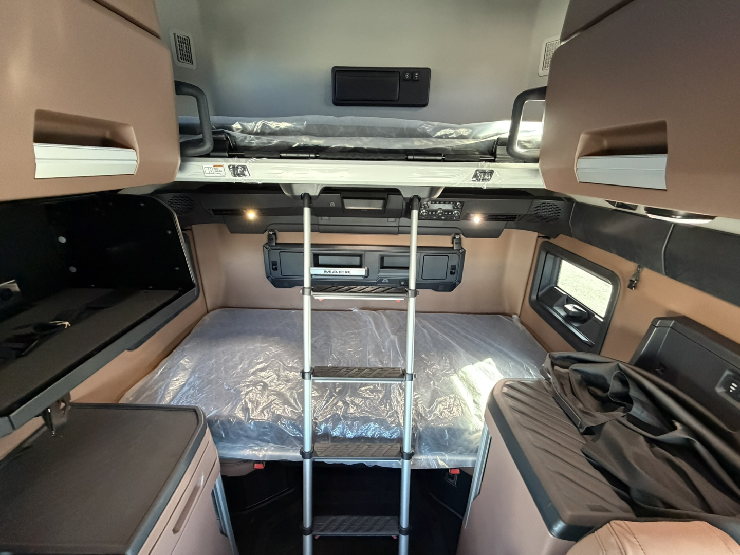 Interior of a 2026 Mack PR64T76H sleeper cab with bunk bed, ladder, and control panel visible.