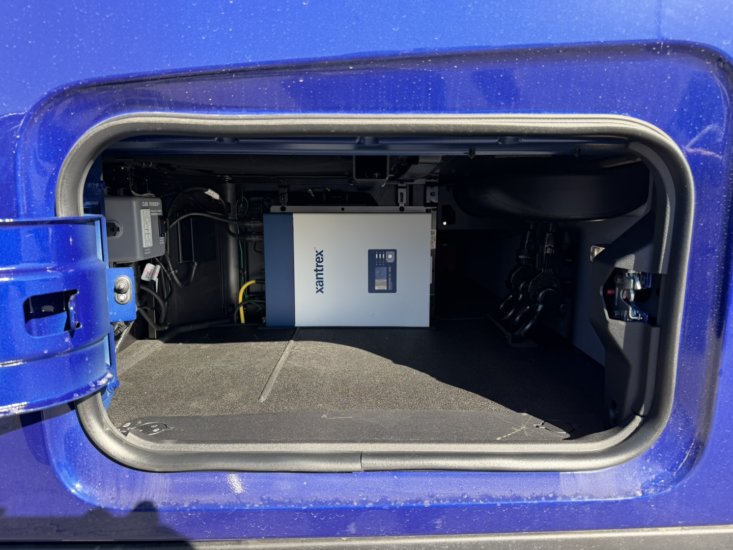 Truck compartment showing Xantrax power inverter mounted inside storage bay of a blue Mack PR64T76H.
