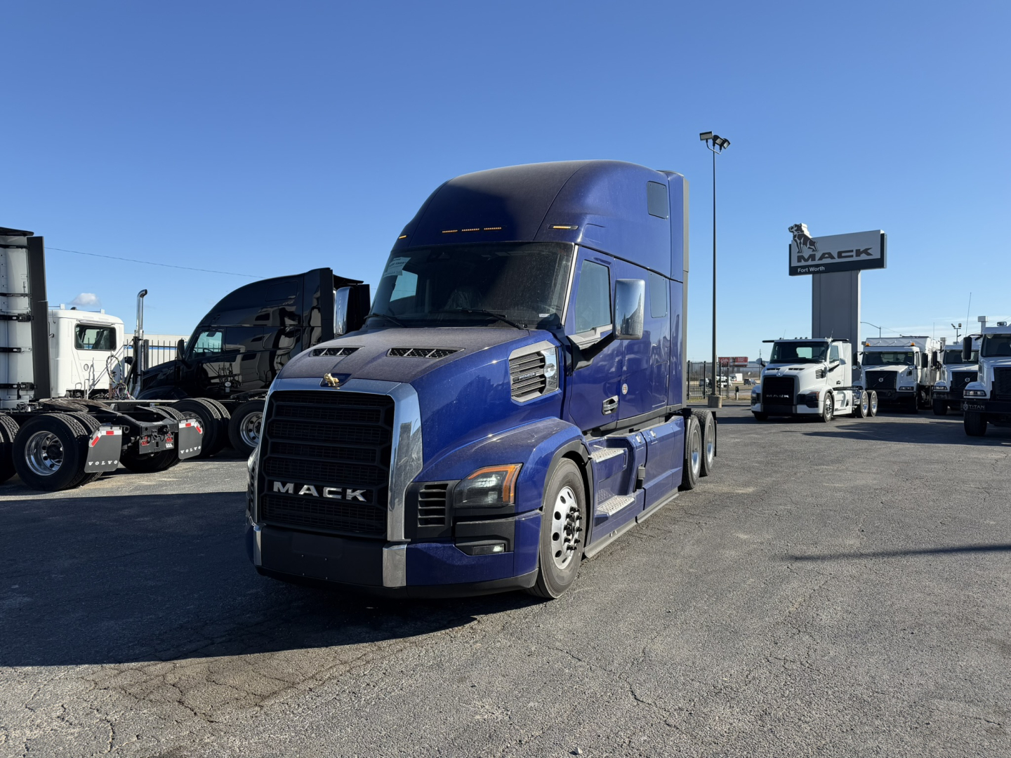 Mack PR64T76H truck in blue in a dealership lot showing front view with chrome grille and Mack sign in background.