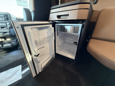 Mini-fridge and freezer in a Mack PR64T76H cab interior showing open fridge and small freezer compartment.