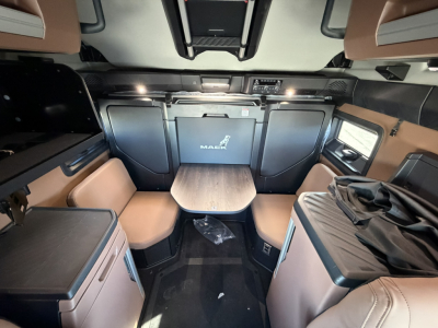 Interior view of a new Mack PR64T76H sleeper cab showing a table with seating around, cabinetry, and a black panel with a Mack logo.