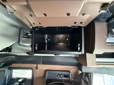 Front console area of a Mack PR64T76H truck cab showing an open overhead storage compartment with a black interior, and a light beige dashboard area.