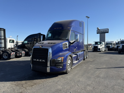 Mack PR64T76H truck in blue in a dealership lot showing front view with chrome grille and Mack sign in background.