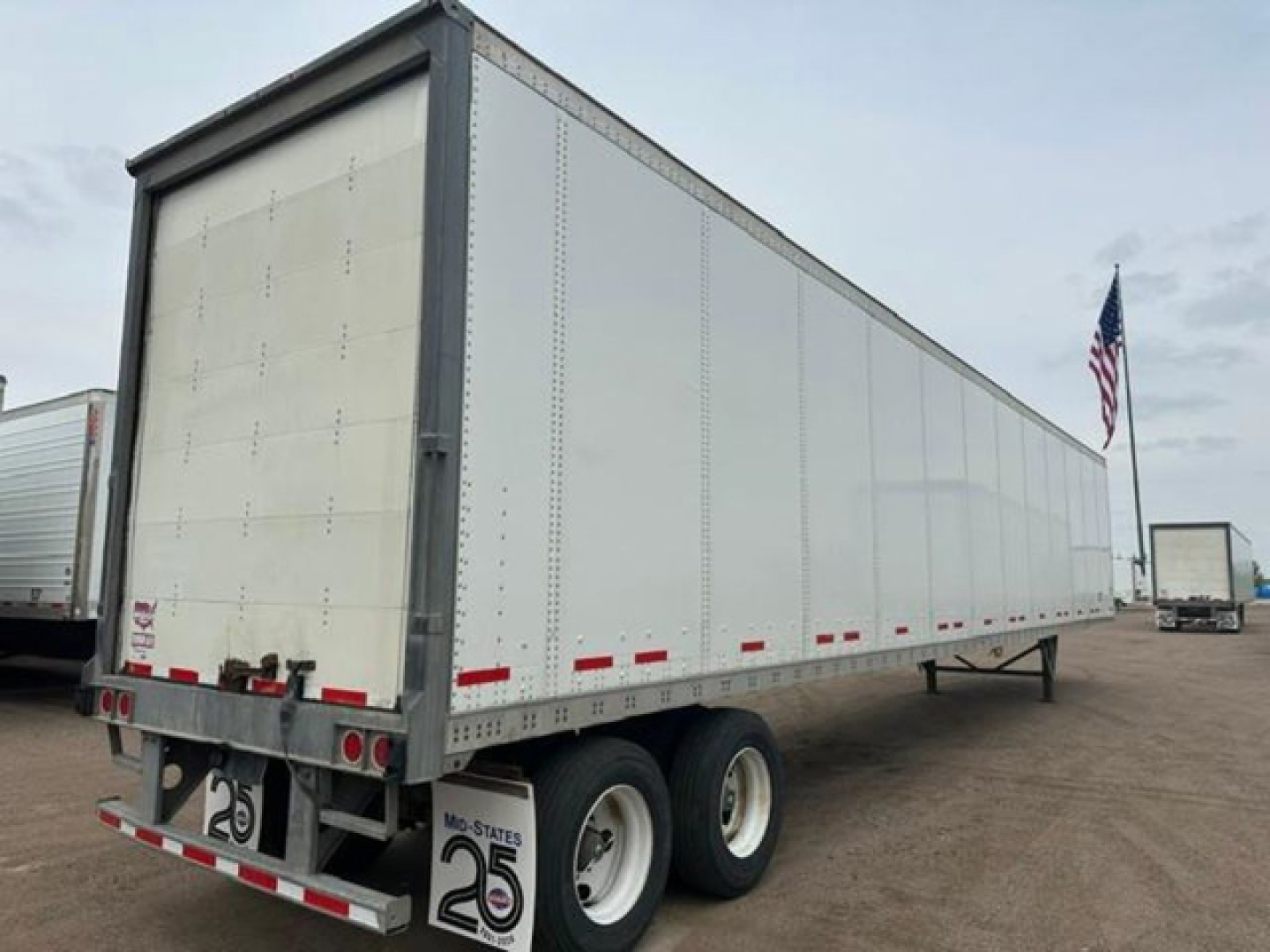 Trailer side view showing a white Wabash van trailer with dual rear axles and a rear door; stock No U90914 visible with U.S. flag in background.