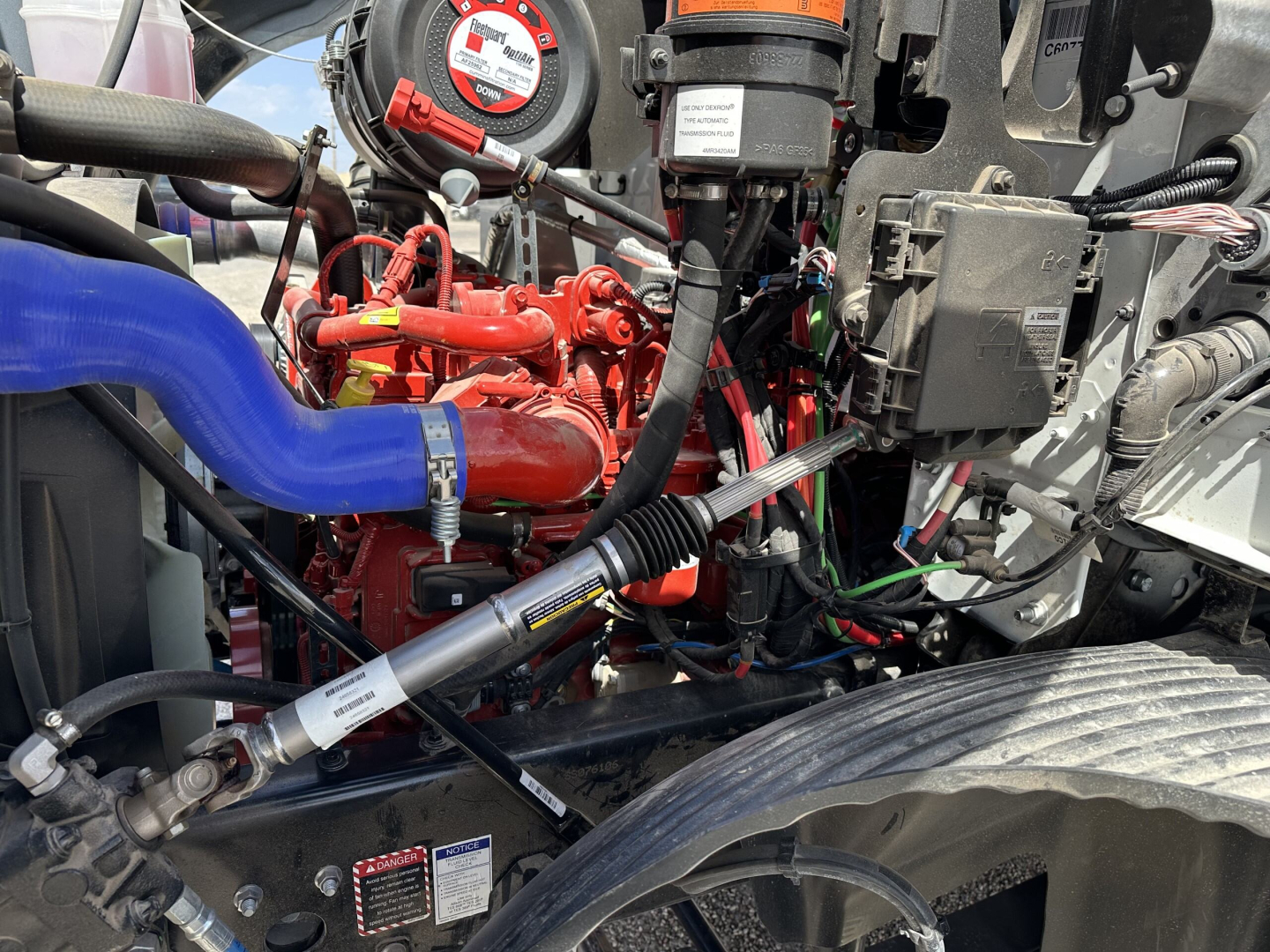Mack MD7 engine bay showing red engine components, blue hose, wiring harness, and various labels/filters.
