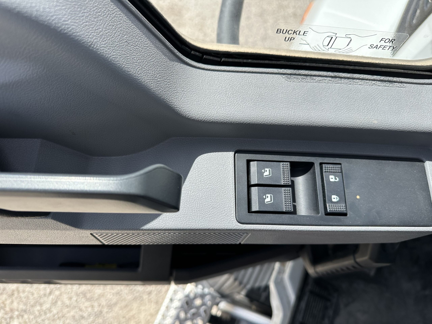 Vehicle interior door panel with window controls; small text visible on window switch area.