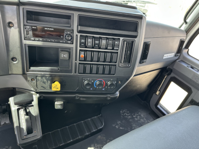 Cab interior of a Mack MD7 truck showing dashboard with stereo, multiple switches, climate controls, and a yellow knob in lower left.