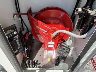 Mack MD7 engine bay view with red fire suppression reel and control hardware; labels and switches visible on metal floor panel.