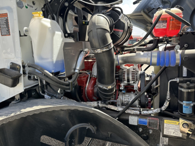 MD7 engine bay showing coolant reservoir, turbo intake piping, belts, alternator, and hydraulic lines in a service truck engine compartment.