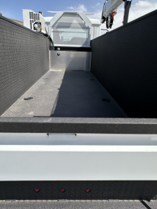 Mack MD7 truck bed area with metal storage compartments and a flat cargo floor, rear view showing sidewalls and tailgate edge.