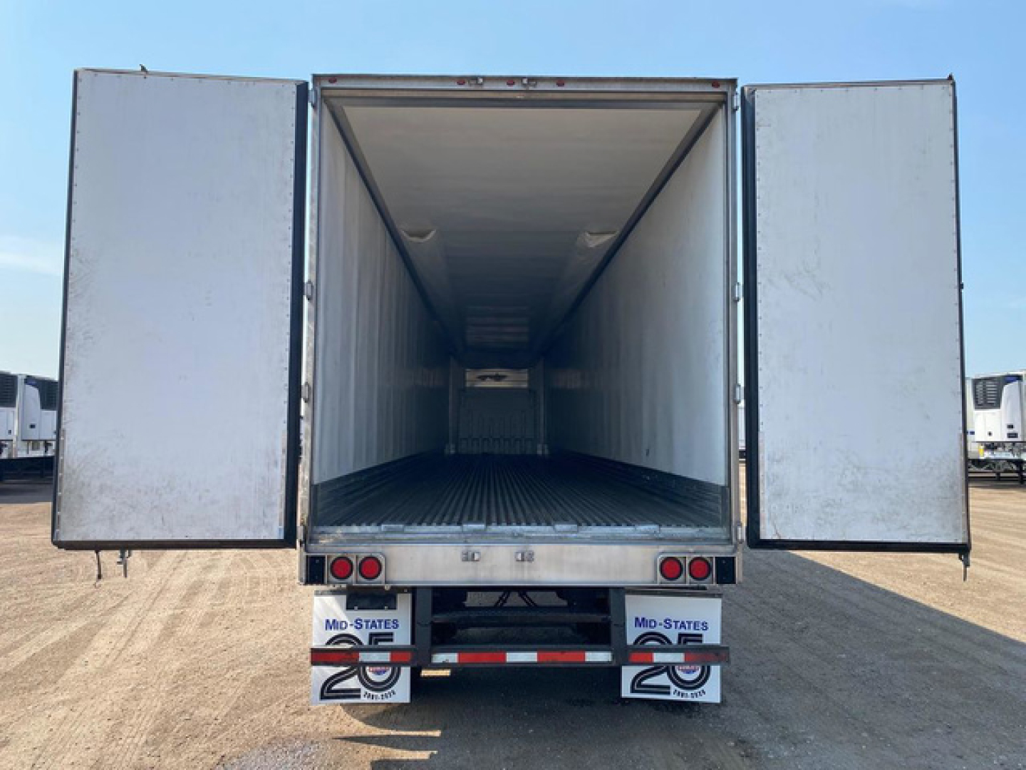 Trailer interior view of a refrigerated utility trailer with rear doors open, empty cargo area, metal floor, and white exterior; U.S. States 20 license plate frames visible on bumper.