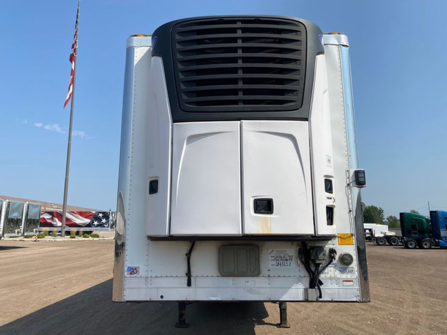 Refrigerated trailer rear view with white body and black cooling unit grille, undercarriage and hitch visible.