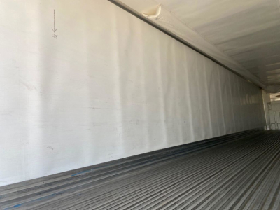 Interior of refrigerated trailer with ribbed metal floor and smooth silver walls. Small marks and a faint arrow near top left. No readable labels or text.
