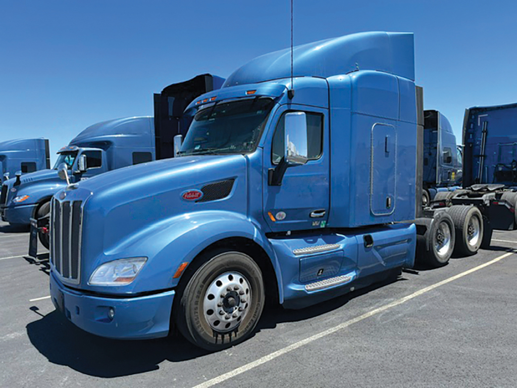 Truck image showing a blue Peterbilt 579 UltraCab tractor, side view with sleeper, chrome grille, large white rear wheels, and tandem axles.