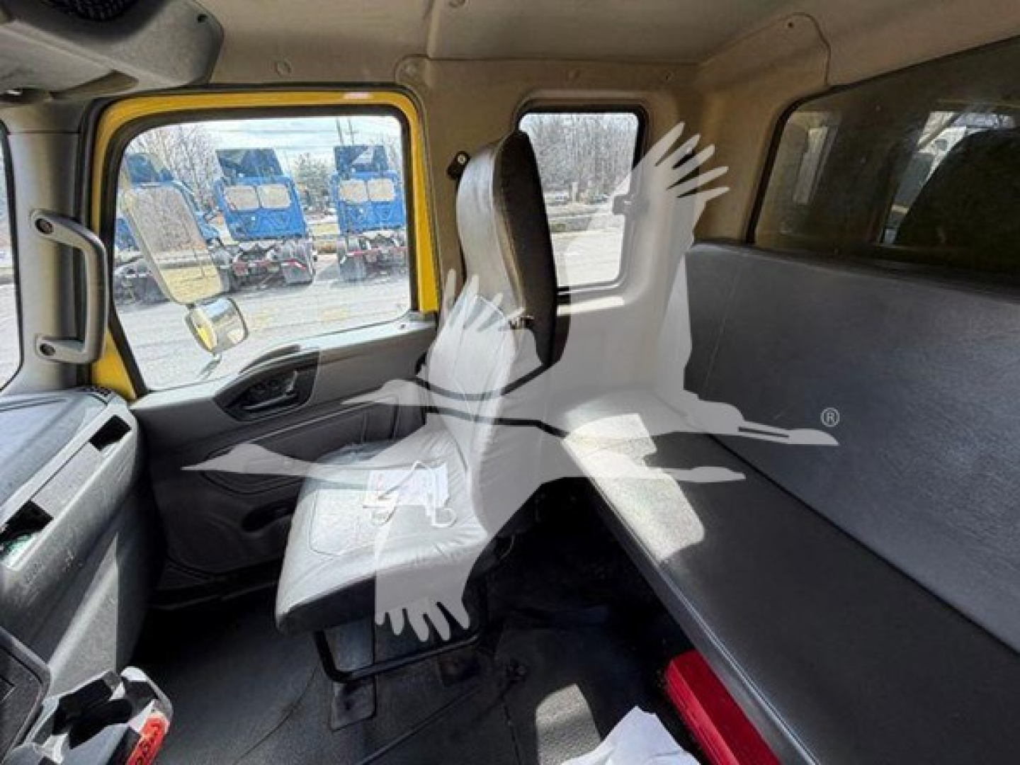 Interior of a 2020 International MV moving van cab view with driver seat and passenger bench, visible side window, yellow door frame, and rear cargo area.