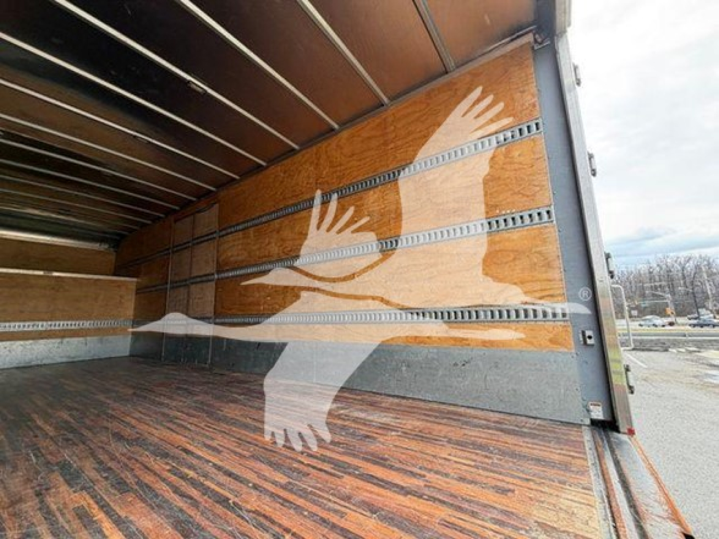 Interior of a moving van cargo area with wooden side walls and metal rails; visible painted dove illustration on the wall.