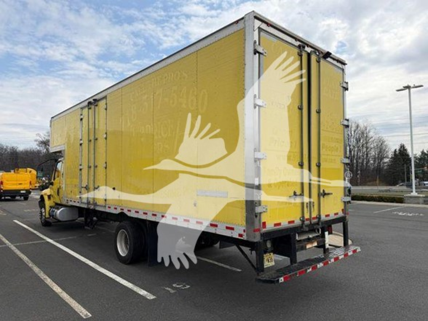 Rear and side view of a yellow moving van truck with a white crane-like bird logo on the side and back doors.