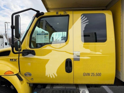 Truck cab side with MV logo and yellow paint, GVW 25,500, black door handle, window, and side mirror.