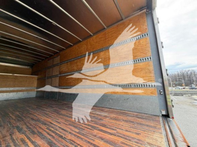 Interior of a moving van cargo area with wooden side walls and metal rails; visible painted dove illustration on the wall.