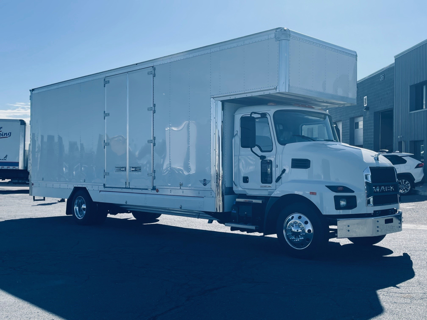Box truck with white cab and large rectangular cargo box, Mack MD6, side view showing cab, front grille, and doors.