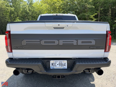 Ford F-150 Raptor rear view showing large FORD lettering on tailgate, dual exhausts, NY license plate, and rear bumper with step.