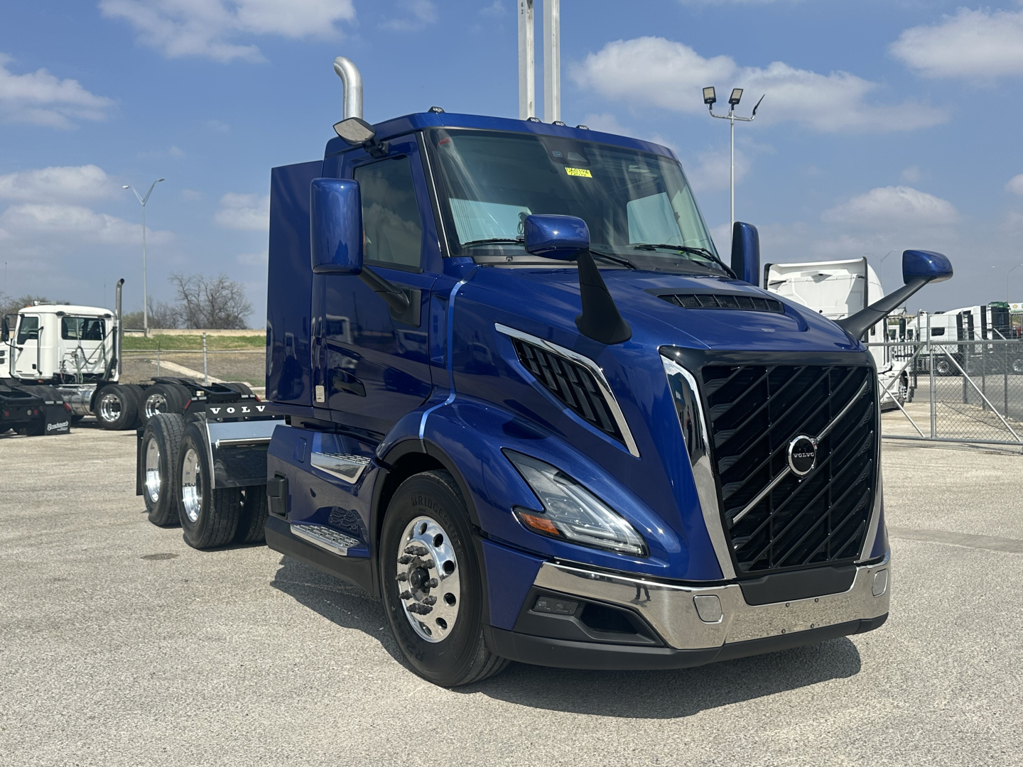Blue Volvo VNR64T300 cab front-left view showing chrome front bumper, large black grille, dual vertical exhaust stacks, aerodynamic mirrors.