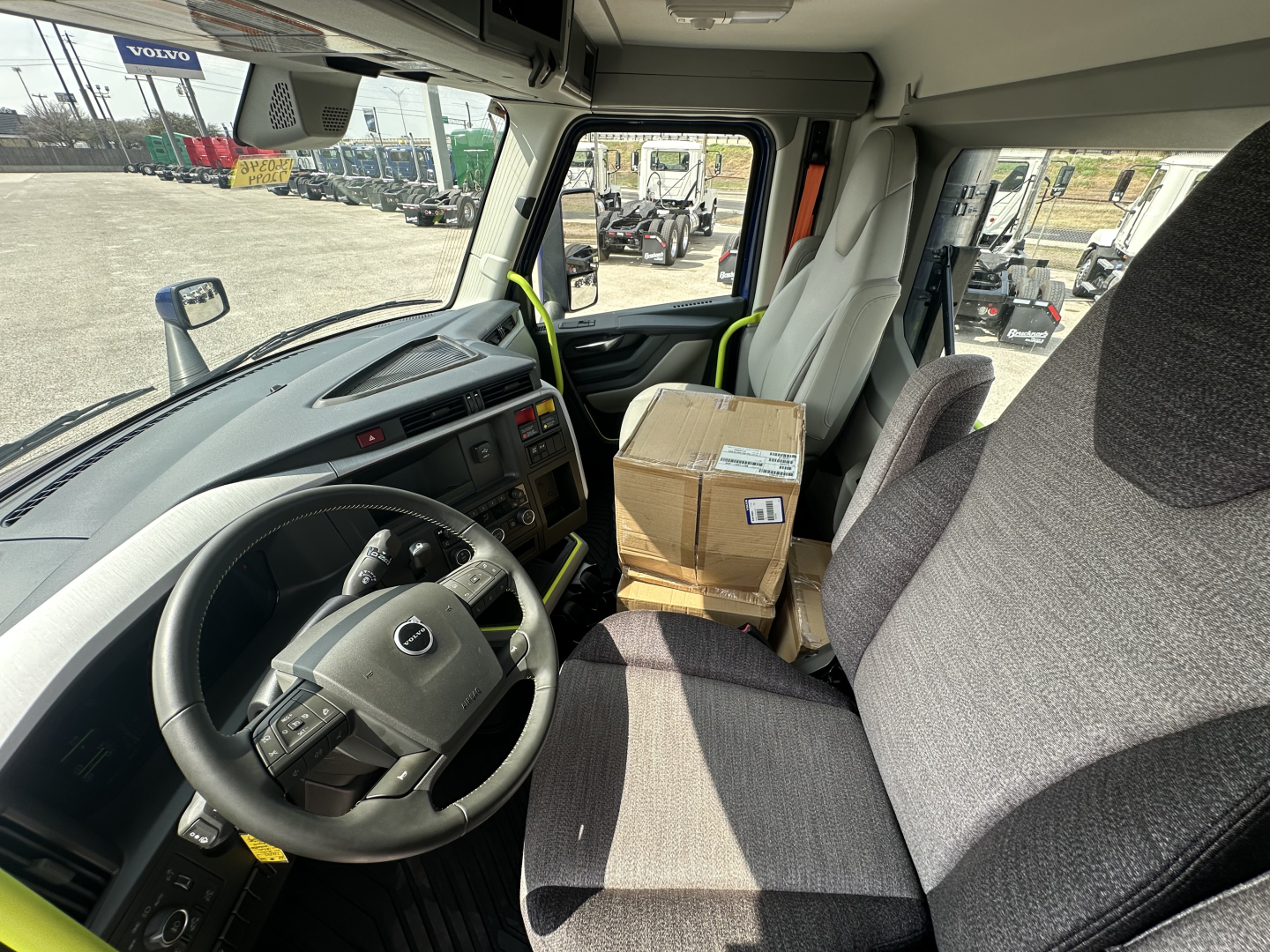 Volvo VNR64T300 truck cab interior showing steering wheel, driver's seat, and a cardboard package on the passenger seat.