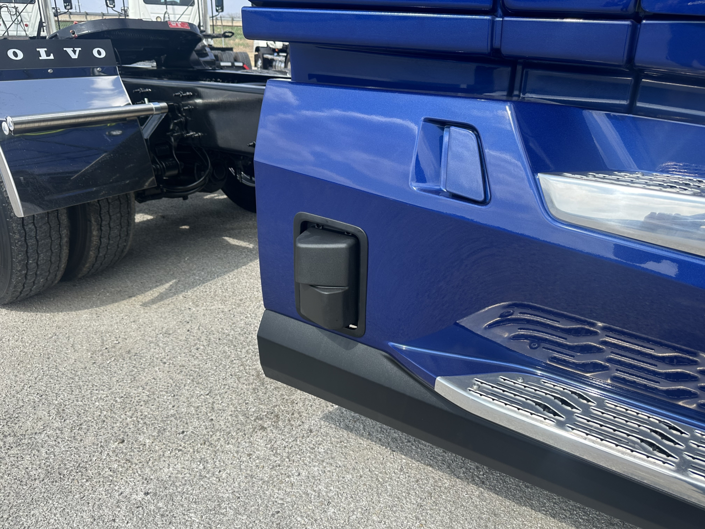 Volvo VNR64T300 truck front bumper area with blue paint, black step, and part of the grille visible.