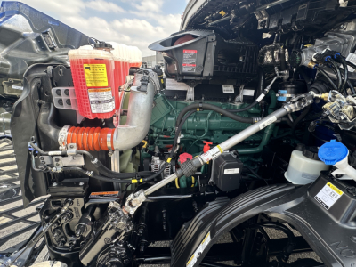 Volvo VNR engine bay showing coolant reservoir, air intake, hoses, wiring, and green engine block in daylight