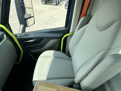 Interior of a new Volvo VNR64T300 truck cab with light gray seats, black dashboard, neon green accents on door handles and grab bars. Side mirror visible through window.