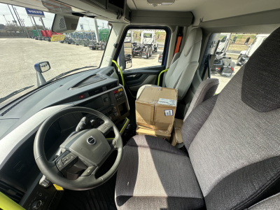 Volvo VNR64T300 truck cab interior showing steering wheel, driver's seat, and a cardboard package on the passenger seat.