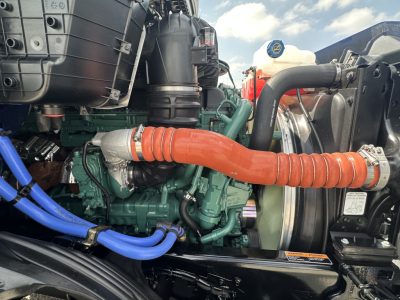 Volvo VNR64T300 engine bay showing green diesel engine with orange corrugated intake hose, blue coolant hoses, black plastic air intake, radiator fins, and various metal components.