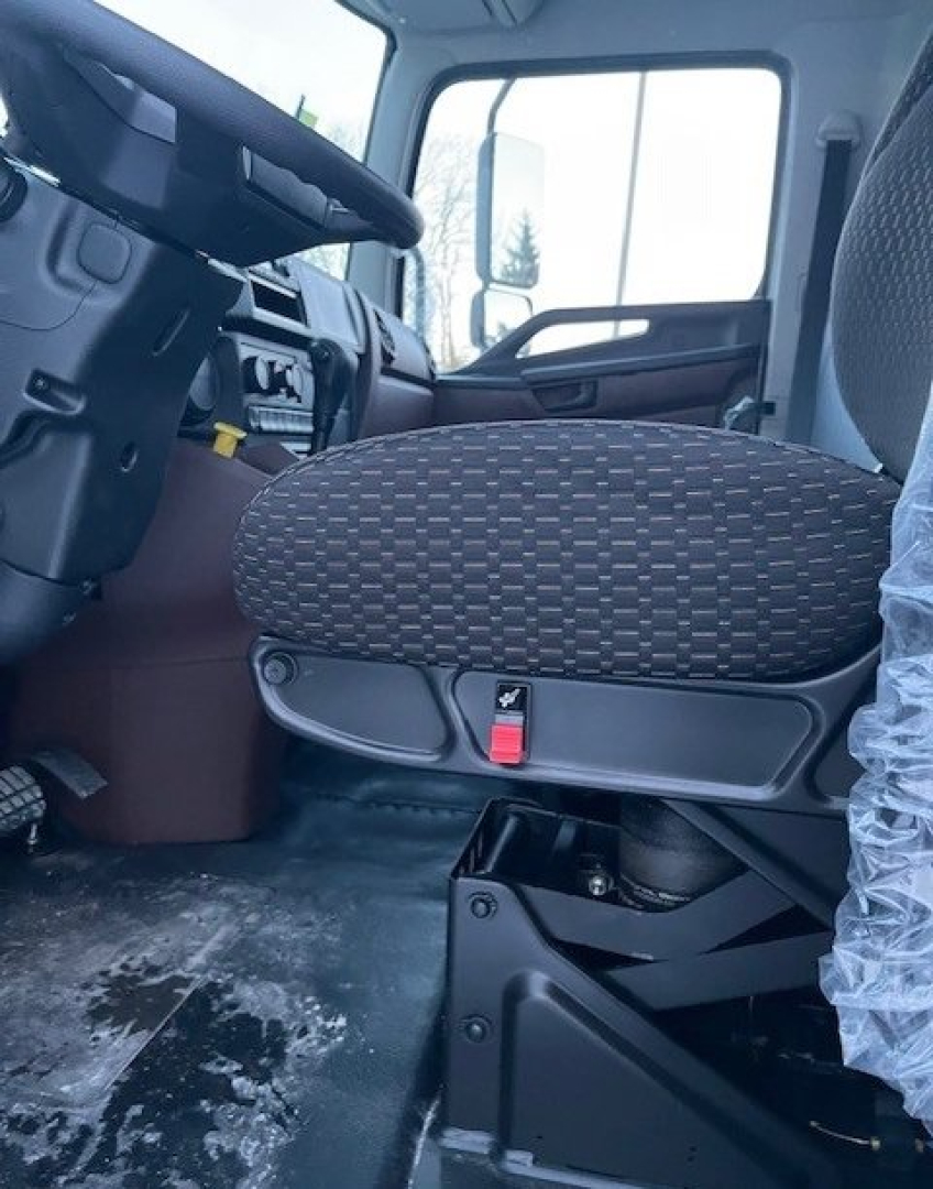 Cab interior of a 2026 Hino L6 box van showing driver seat with fabric upholstery and seat adjustment lever; dashboard and steering wheel visible in background.