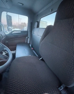 Truck cab interior showing front driver seat and passenger seat with fabric upholstery; dashboard and steering wheel visible; window and door pane; minimal view of exterior.