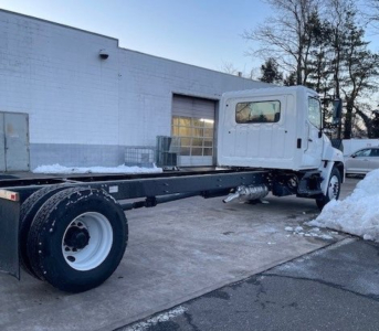 Truck chassis showing cab and long wheelbase frame from the right-rear angle; white cab, black chassis, snow on ground.