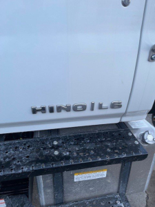 Truck side showing 'HINO 16' badge on cab, metal step rail with moisture and grime, white cab paint, part of door and hinge visible.
