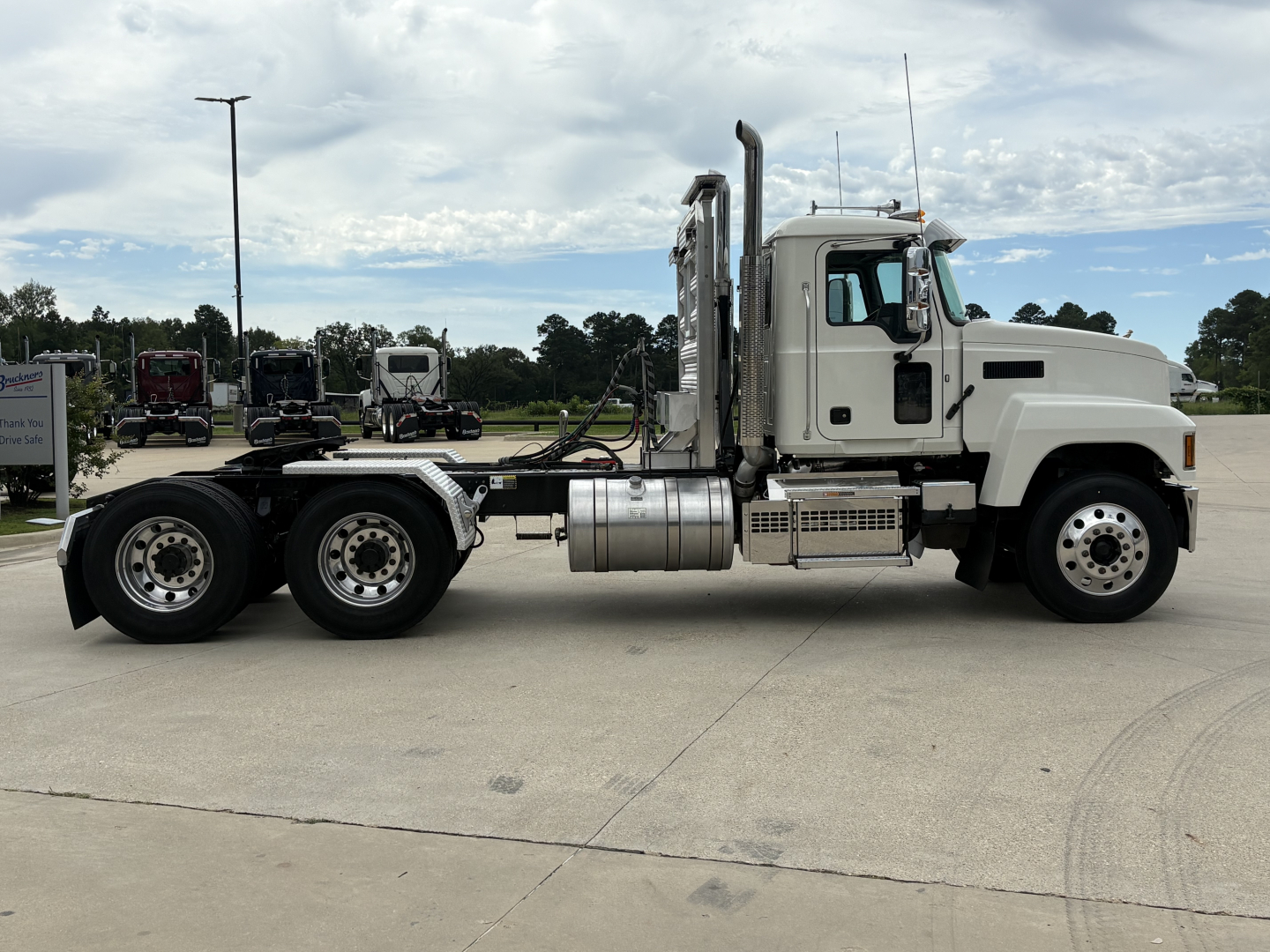 Truck side view of a white 2026 Mack PI64T conventional daycab showing chassis, dual rear axles, and exhaust stacks.