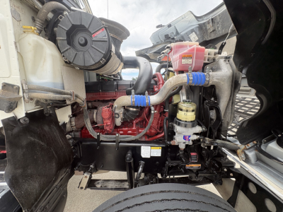 Mack PI64T engine bay showing red engine block, blue silicone hoses, black air intake, coolant reservoir, and various hydraulic lines.