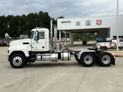 2026 Mack PI64T conventional daycab truck side view showing cab, exhaust stacks, fuel tanks, and 6x4 rear tandem wheels in front of service bay.