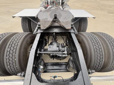 Underbody view of a new 2026 Mack PI64T conventional daycab showing the chassis with drive axles, suspension, differential, and mud flaps.