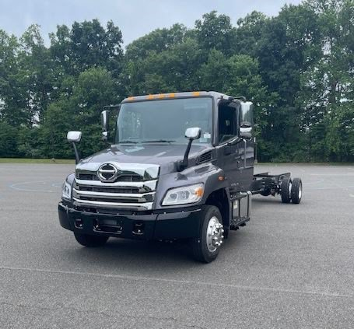 Hino L6 cab chassis truck front view with chrome grille, side mirrors, and orange cab roof marker lights in a parking lot.