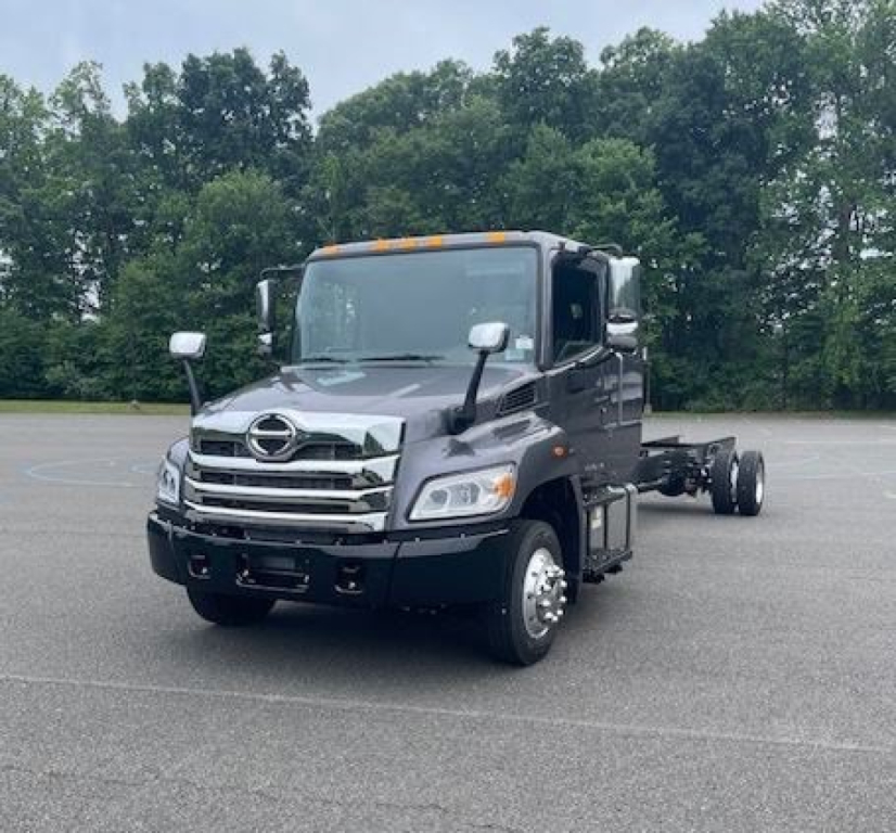 Hino L6 cab chassis truck front view with chrome grille, side mirrors, and orange cab roof marker lights in a parking lot.